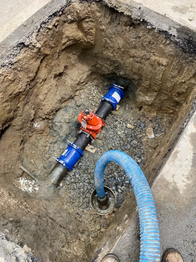 Water main pipe and valves in an open hole dug in the pavement.